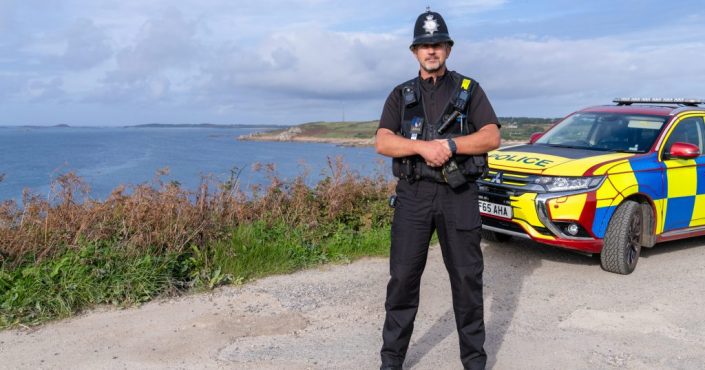 Isles of Scilly Sergeant Al Jordan stood by his police car against the scenic backdrop of the island