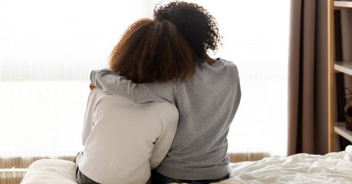 A mum and daughter shown hugging on a bed with their backs to the camera
