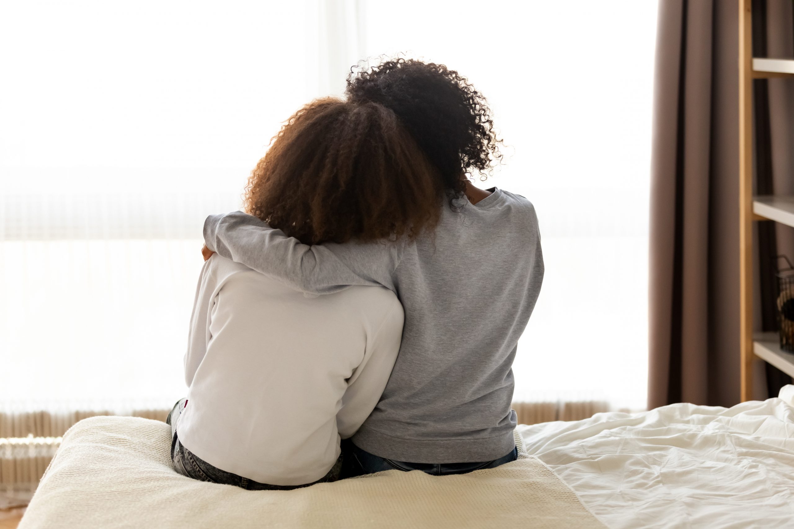 A mum and daughter shown hugging on a bed with their backs to the camera